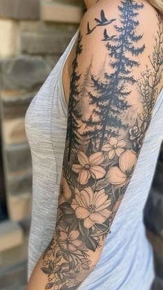 a woman's arm with flowers and birds in the woods on her left arm