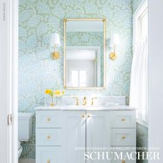 a white bathroom with blue wallpaper and gold accents