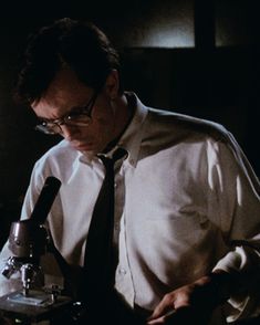 a man wearing glasses and a tie is looking at something in front of a microscope