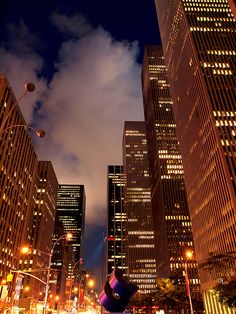 the city is lit up at night with clouds in the sky and skyscrapers on both sides