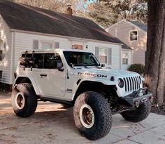 a white jeep parked in front of a house with large tires on it's wheels