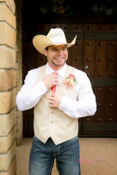 a man in a cowboy hat and vest is holding onto his tie while standing outside