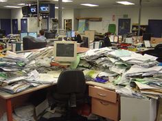 a woman standing in an office surrounded by piles of papers and clutter with her arms outstretched