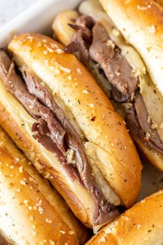 several sandwiches with meat and cheese in a white container