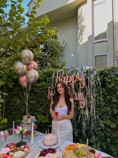 a woman standing in front of a table filled with food and balloons that say happy birthday