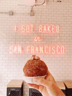 a person holding up a doughnut in front of a neon sign that reads i got baked in san francisco