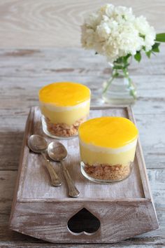 two desserts are sitting on a tray with spoons and flowers in the background