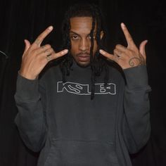 a man with dreadlocks standing in front of a black curtain holding his hands up