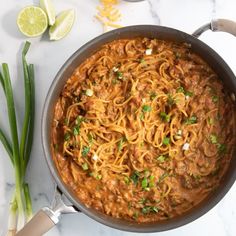 a skillet filled with noodles and meat on top of a table next to green onions