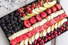 an assortment of fruits and berries arranged in a rectangular tray on a white tablecloth