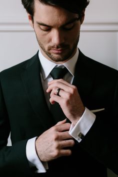 a man adjusting his tie while wearing a black suit and white shirt with a pocket square