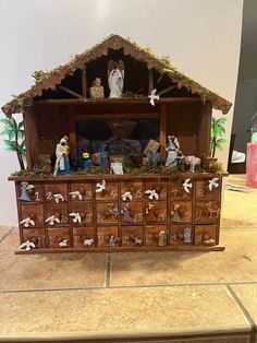 a nativity scene with figurines on top of a wooden cabinet in the middle of a tiled floor