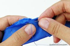 someone is sewing something on a blue piece of cloth with scissors and thread in their hands