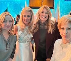 three women standing next to each other in front of a blue curtain and chandelier