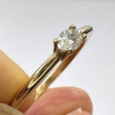 a close up of a person's hand holding a ring with a diamond on it