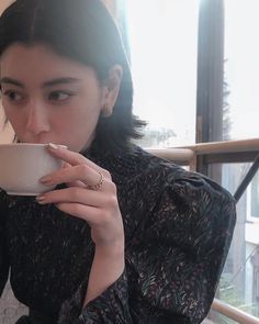 a woman sitting at a table drinking out of a cup with her hand on the coffee mug