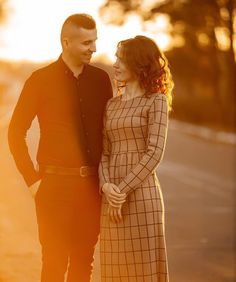 a man and woman standing next to each other in front of the sun at sunset