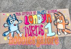 there is a sign on the sidewalk that says loony turns 1 and has two cats