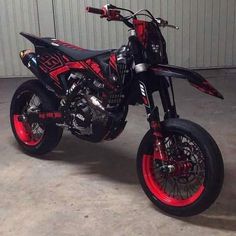 a red and black dirt bike parked in front of a garage door on concrete floor