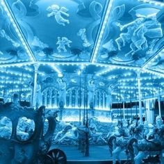 an illuminated merry go round at night with horses and people on the carousel in blue