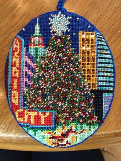 a cross stitch christmas ornament hanging from a wooden chair with a city scene on it