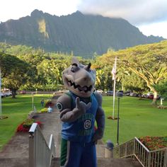 a person in a dinosaur costume is standing on the steps to a park with mountains in the background