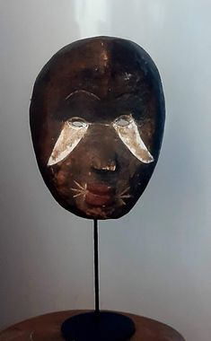 a wooden mask on a metal stand in front of a white wall