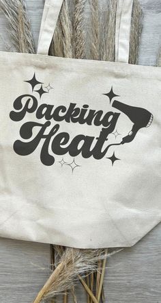 a tote bag with the words packing heat printed on it next to dried grass