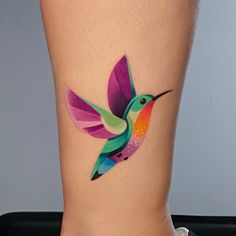 a colorful hummingbird tattoo on the side of a woman's leg, with watercolors