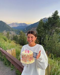 a woman is holding a cake with candles on it and giving the thumbs up sign