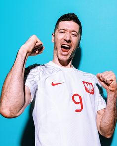 a man with his fist up in front of a blue background wearing a white shirt