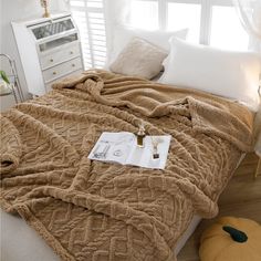 a bed covered in a brown blanket next to a white dresser and window sill