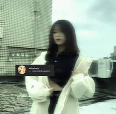 a woman standing in front of a building wearing a white coat and black shirt with her hands on her hips