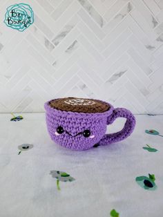 a crocheted coffee cup sitting on top of a white cloth covered tablecloth