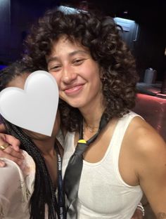 two women posing for the camera with one holding a heart shaped object