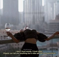 a woman holding a glass of wine on top of a balcony next to a city