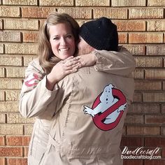 a man and woman hugging each other in front of a brick wall with ghost stickers on it