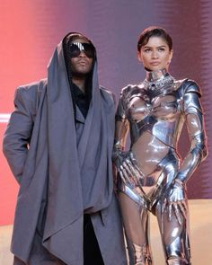 a man standing next to a woman in a futuristic suit