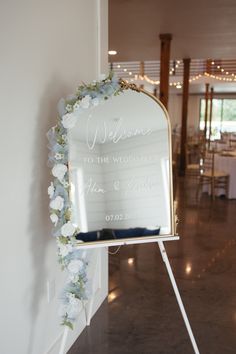 a welcome sign with flowers on it in front of a door at a wedding reception