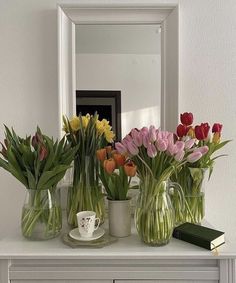 vases filled with tulips and other flowers sit on a table in front of a mirror