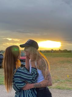 a man and woman standing next to each other in front of a field at sunset