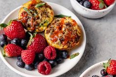 two white plates topped with muffins and berries next to another plate filled with fruit