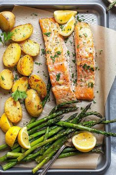 salmon, potatoes and asparagus on a baking sheet with lemon wedges for garnish