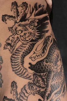 a man's back with tattoos on his arm and shoulder, showing an image of a dragon