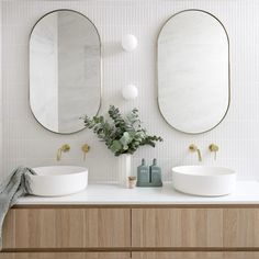 two round mirrors are on the wall in this bathroom, and there is also a vase with flowers