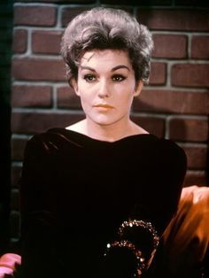 an old photo of a woman with short hair wearing a black dress and diamond brooch