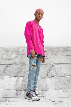 a young man standing on top of a cement slab wearing a pink shirt and ripped jeans