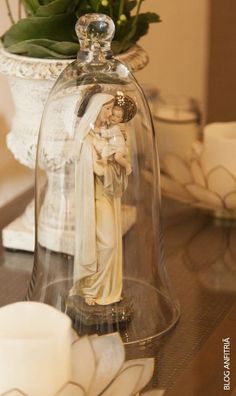 a glass bell jar with a statue under it on a table next to a flower pot