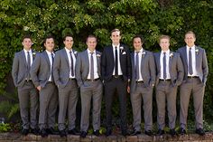 a group of men standing next to each other in front of a green wall and bushes