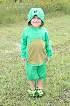 a young boy wearing a green costume standing in the grass with his hands on his hips